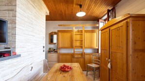 Una cocina con armarios de madera, una mesa de madera con un cuenco de fruta y un televisor en la pared.