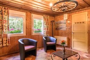 A wooden-paneled room with two leather chairs, a table with a vase, and a large window with curtains.