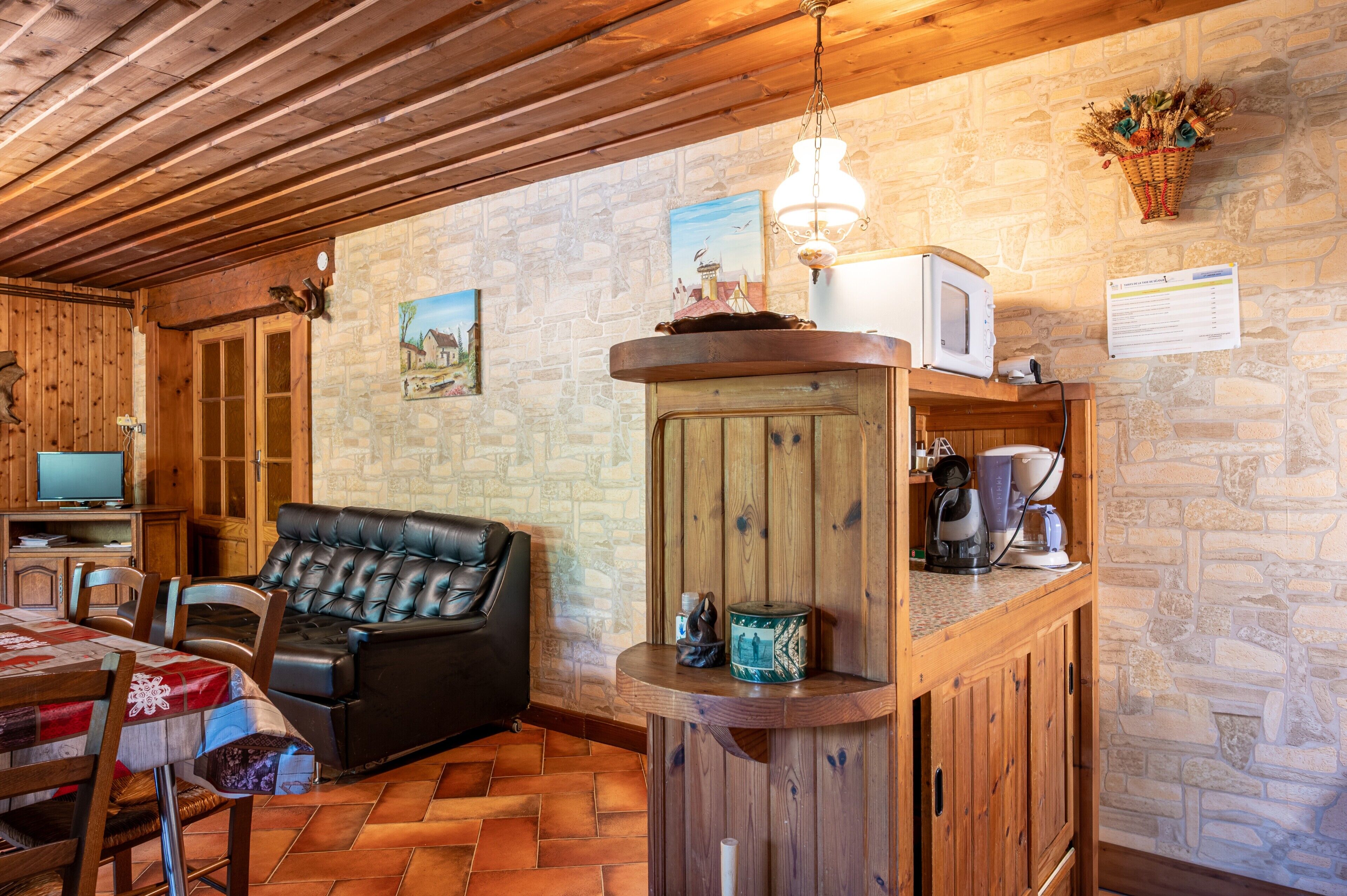 A cozy living area with a leather sofa, wooden furniture, a stone wall, and a mounted television.
