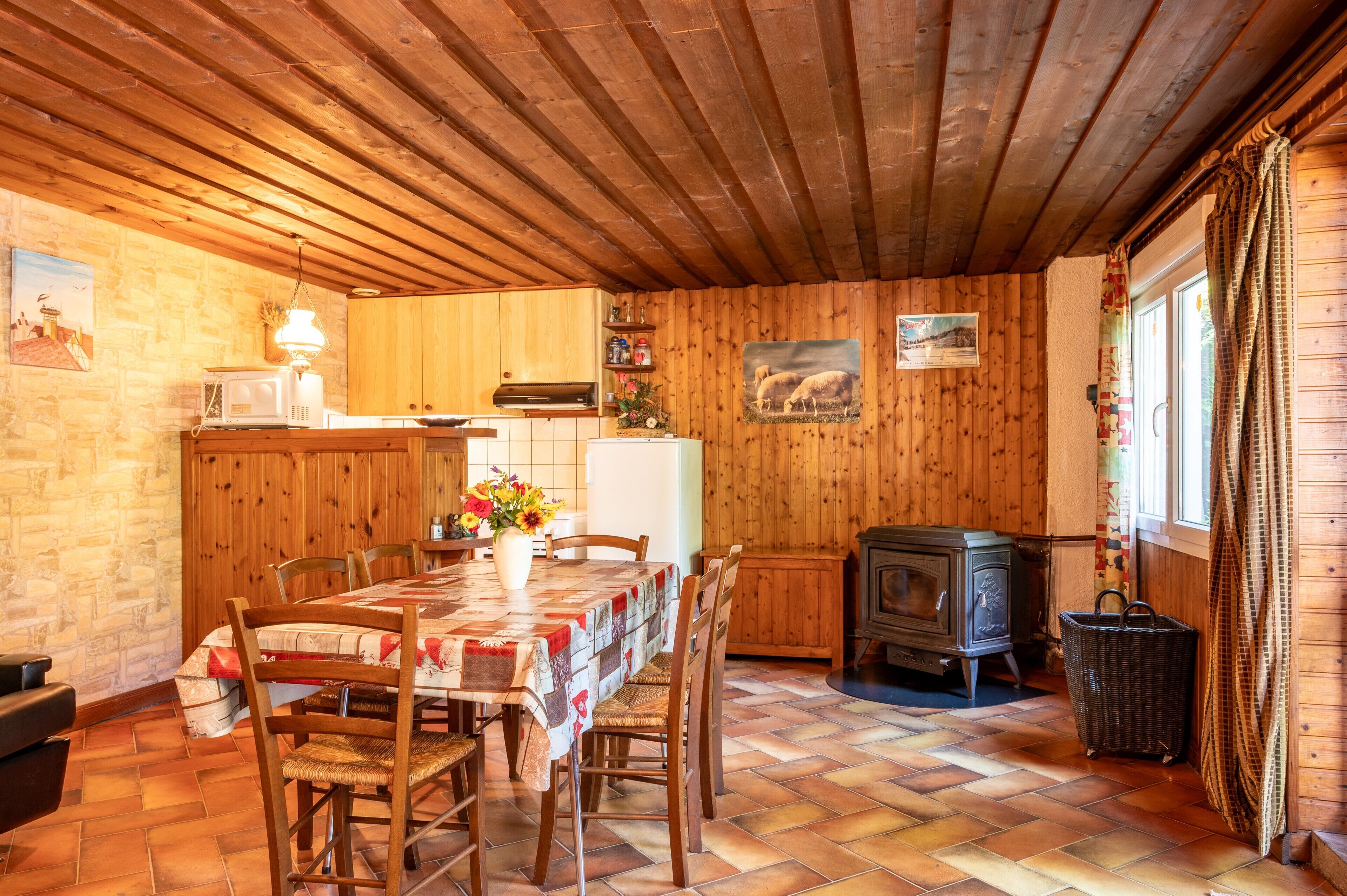 Un interior de madera con una mesa de comedor, sillas, una zona de cocina y un estufa de leña.