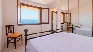 Quarto com cama, uma cadeira, janela com vista para o mar e espelho.
