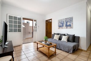 A living room with a sofa, a coffee table, a TV, and a door leading to an outdoor area.