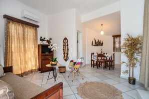 A living room with a sofa, a TV, a dining table with chairs, a decorative mirror, and a potted plant.