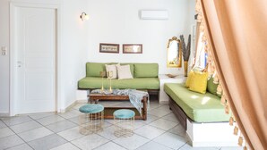 Una habitación con un sofá verde, una mesa de centro de madera, dos taburetes, una puerta blanca y un espejo en la pared.