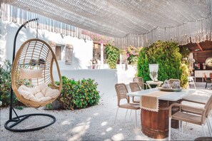 Une terrasse avec un fauteuil suspendu, une table avec des chaises et un mur végétalisé.