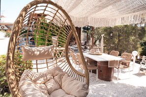 Une chaise en osier avec un coussin, une table en bois et des chaises, le tout installé dans un espace extérieur.