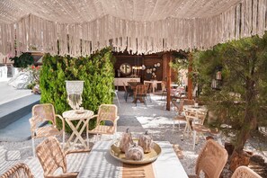 Un espace extérieur aménagé avec des chaises en osier, une table ronde agrémentée d’un vase décoratif et un décor de verdure en arrière-plan.