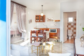 Cocina luminosa con armarios de madera, comedor con sillas y mesa, y baño con inodoro y lavamanos.