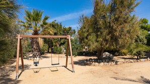 A swing set in a garden with trees and a stone wall. - Apartment In A Hotel 'Sun Rock Boutique - Villa Gerani' with Private Terrace and Air Conditioning (Naxos)