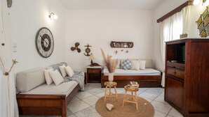 A cozy room with a bed, a sofa, a wooden cabinet, a wall clock, and a small table with a vase.