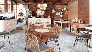 A rustic dining area with a wooden table and wicker chairs, a hanging light fixture, and a brick wall with decorative plates.