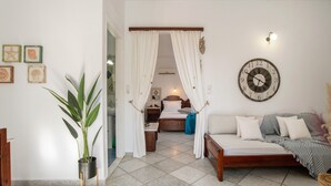 A room with a bed, a sofa, a potted plant, a wall clock, and a door with curtains.