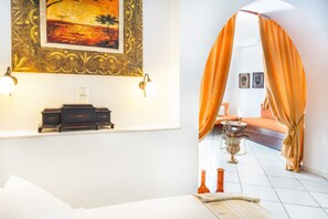 Une pièce comprenant un lit, une table de chevet, une lampe fixée au mur, un tableau encadré et une fenêtre avec des rideaux.
