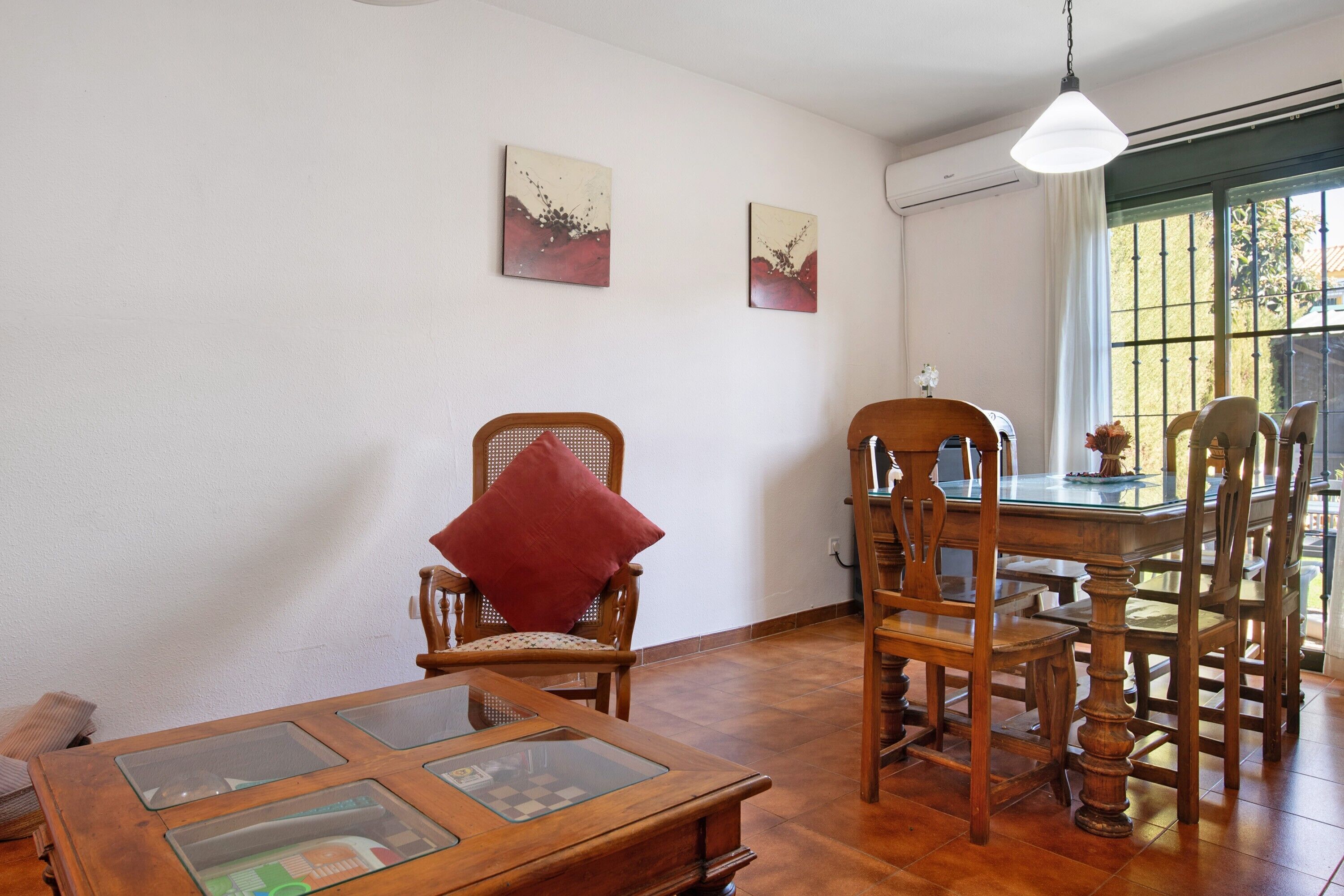 Un comedor con mobiliario de madera, una mesa de vidrio y dos cuadros en la pared.