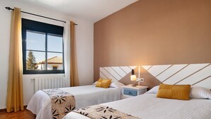 Une chambre d’hôtel avec deux lits, une fenêtre avec des rideaux, une table de chevet avec une lampe et une vue sur un bâtiment à l’extérieur.