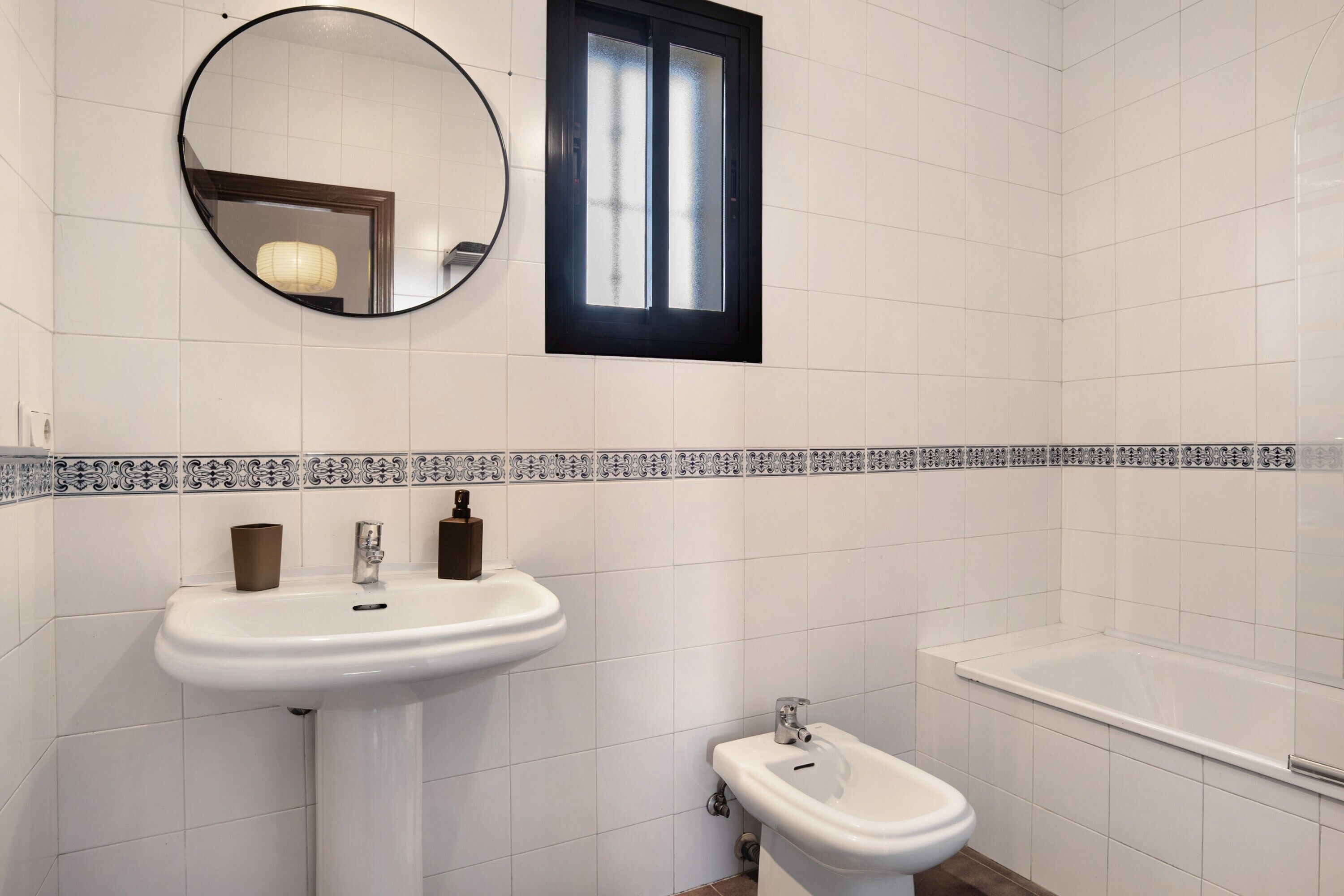 Un baño con lavamanos pedestal, un bidé, un espejo y una ventana.