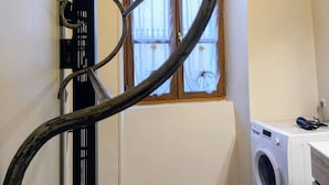Un lavadero con lavadora, una ventana con cortinas y un tendedero de metal.