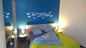 Un dormitorio con cama, lámparas de noche, un espejo y una pared con una frase decorativa.