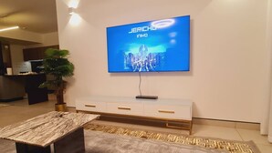 A modern living room with a flat-screen TV mounted on the wall, a wooden coffee table, a white console table, and a patterned rug. - Luxury Modern 3bdr with a pool and  gym (Nairobi)