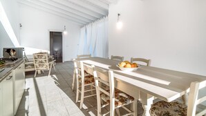 Un espace repas avec une longue table, des chaises et un saladier rempli de fruits.