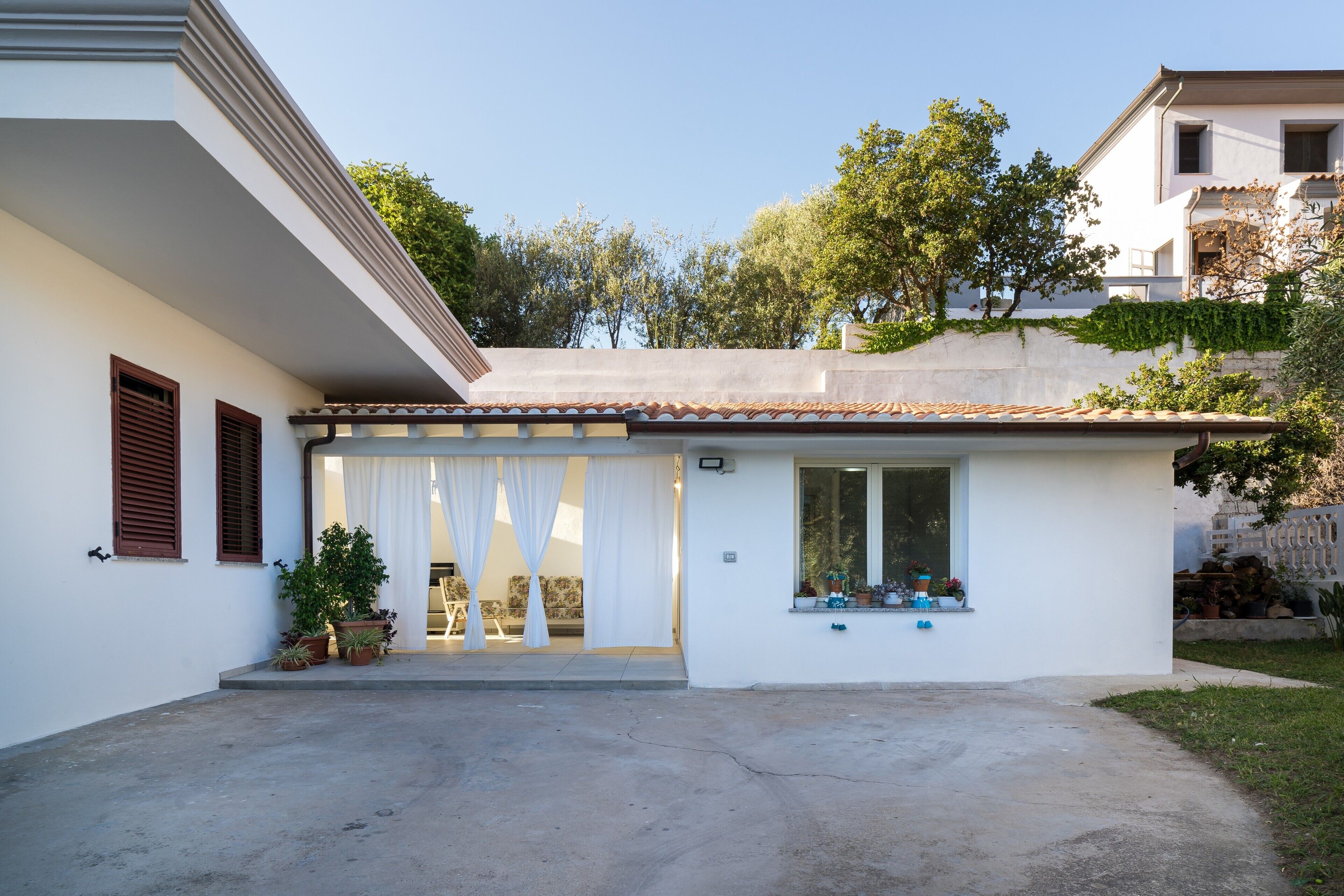 A single-story house with a covered patio, a small window with plants, and a concrete driveway.