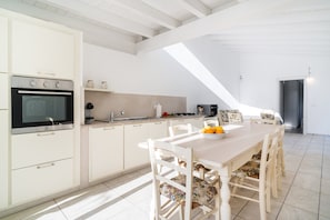 A modern kitchen with white cabinetry, a dining table with floral chairs, and a skylight. - Holiday Home 'Domo Bonaeras' with Mountain View, Wi-Fi and Air Conditioning (Irgoli)