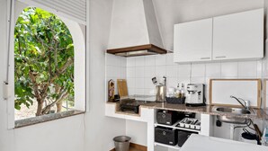 Een keuken met witte kastjes, een roestvrijstalen spoelbak, een koffiezetapparaat en een raam met uitzicht op een boom.