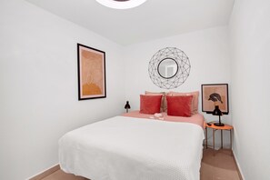 A bedroom with a bed, a round mirror, a framed picture, and a small table with a lamp.