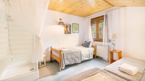 Une chambre avec un plafond en bois, une fenêtre avec des rideaux, un lit, une table de chevet et un radiateur.