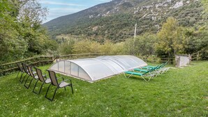 Une serre avec des chaises et une table, entourée d’une clôture en bois, avec une chaîne de montagnes en arrière-plan.