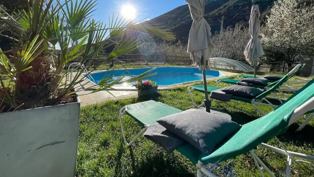 Un espace aménagé au bord de la piscine, avec des chaises longues, une piscine et une chaîne de montagnes en arrière-plan.