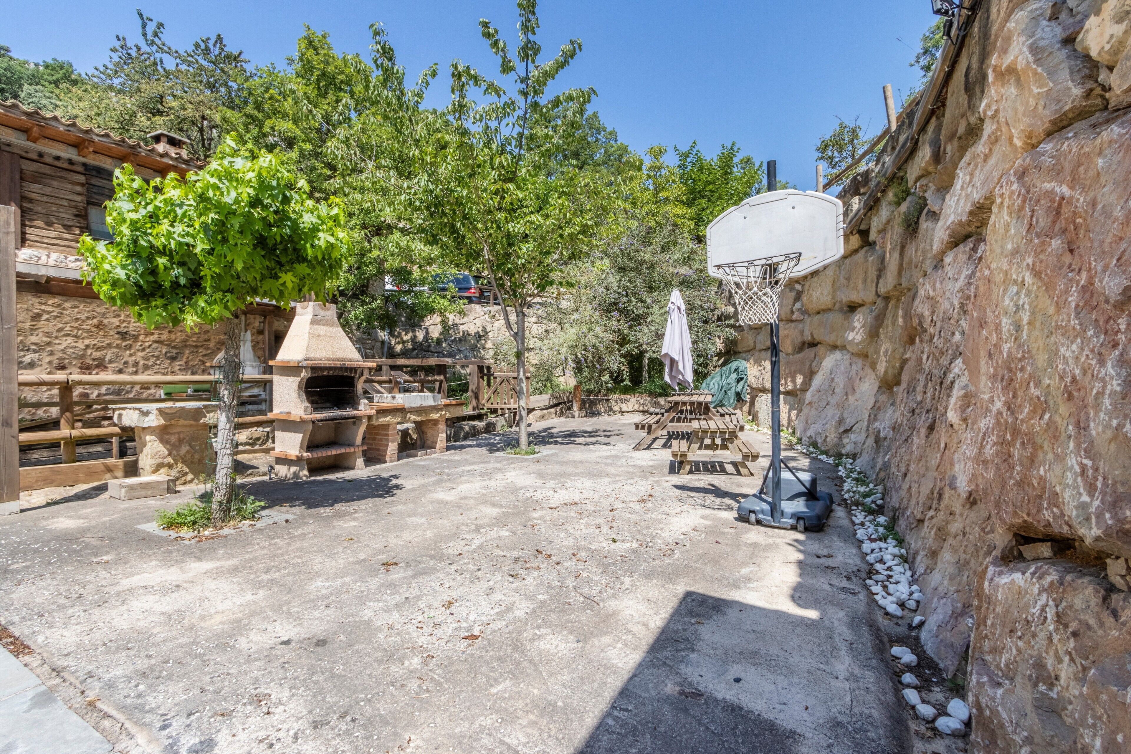 Un patio al aire libre con pared de piedra, aro de baloncesto y parrilla.