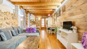 A cozy cabin interior with a wooden ceiling, stone wall, and a dining area with a table and chairs.