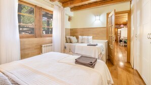 A bedroom with a large bed, a smaller bed, wooden beams, a radiator, and a view of the outside.