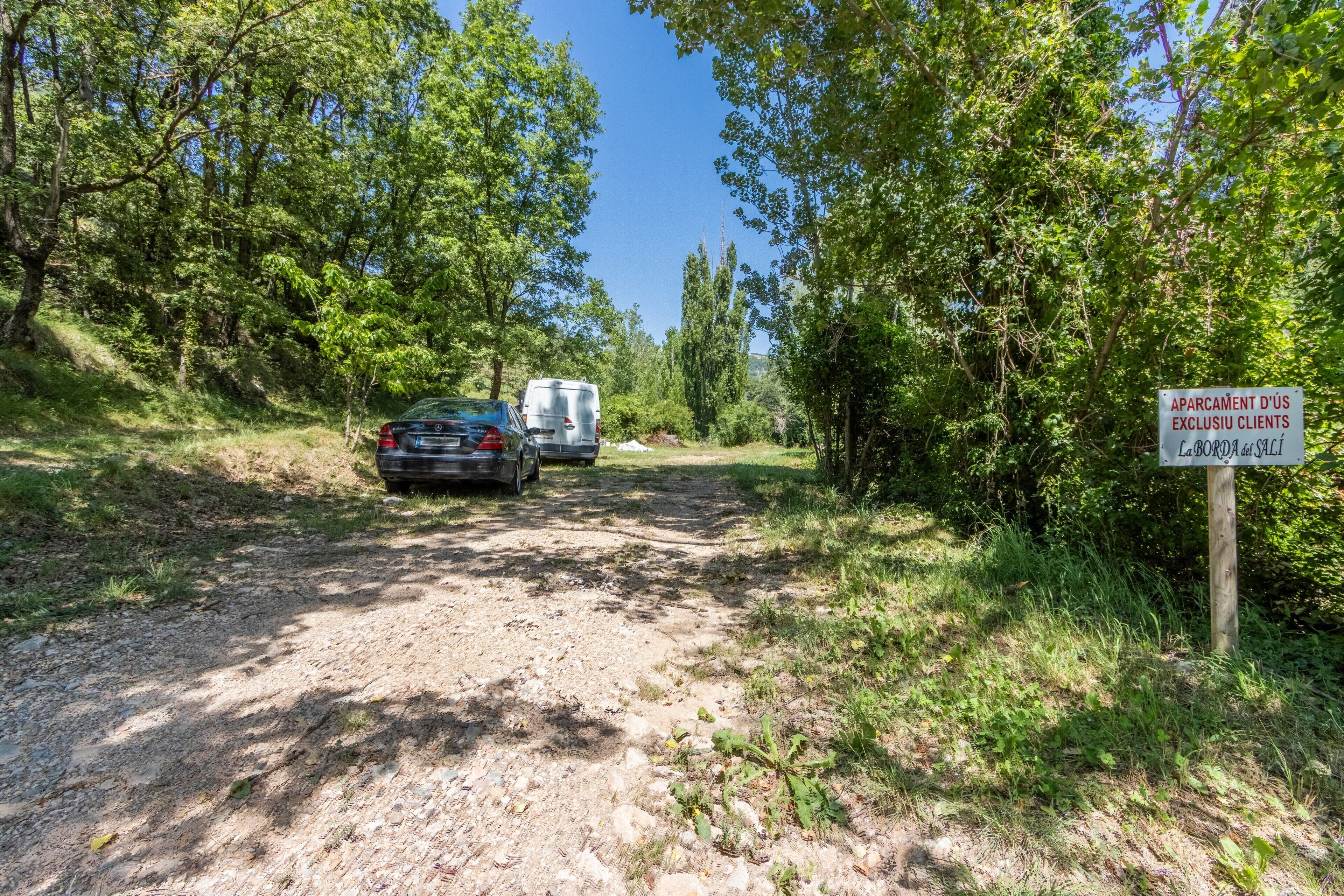 A gravel path with a car and a trailer, surrounded by trees and a sign indicating a private parking area.