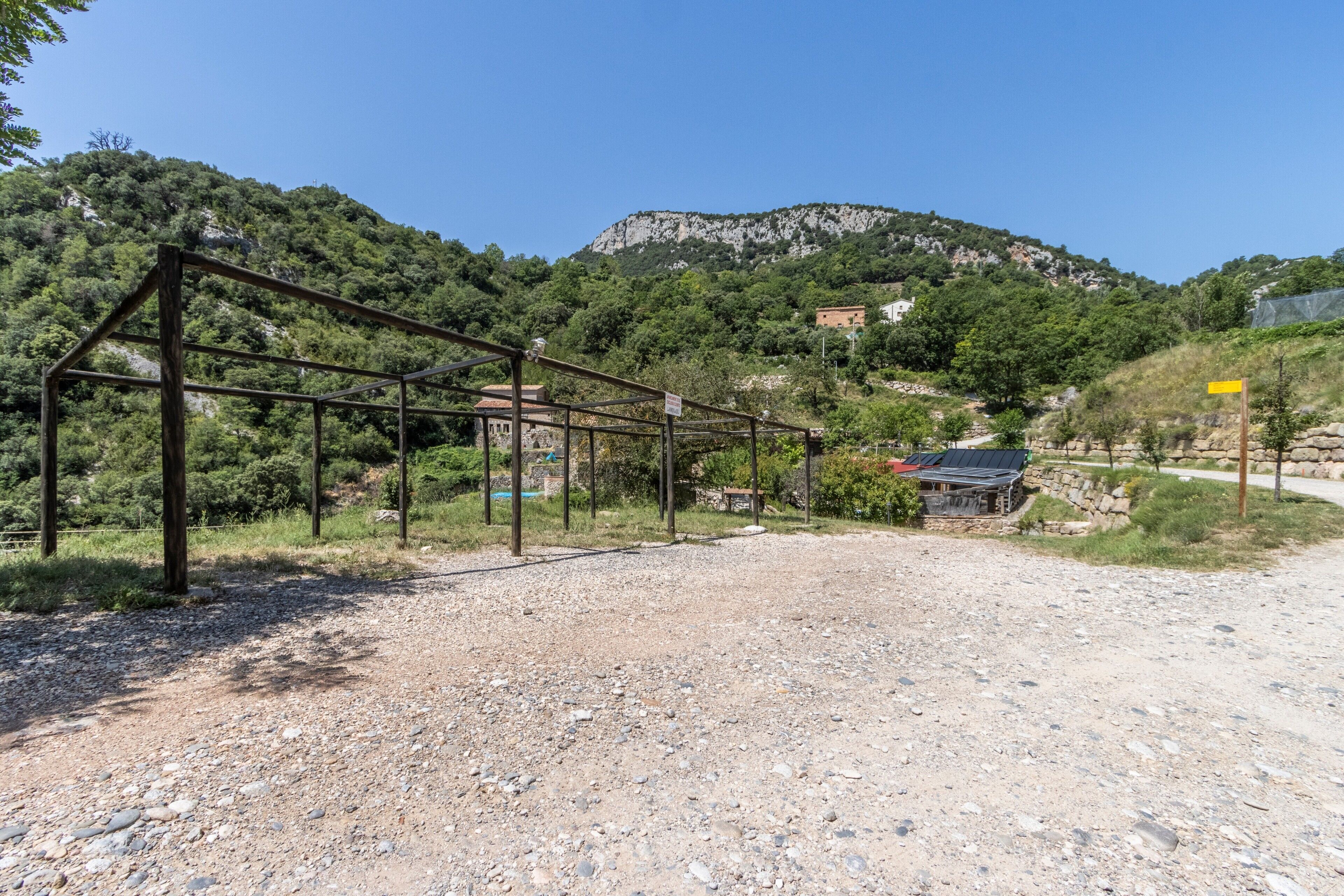 Un chemin de gravier mène à une structure métallique, entourée de verdure et avec une montagne en arrière-plan.