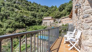 Un balcon avec un mur en pierre, une piscine et des meubles d’extérieur blancs.