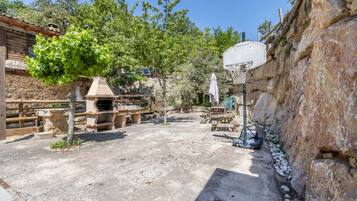 An outdoor patio area with a stone wall, a basketball hoop, and a barbecue grill.