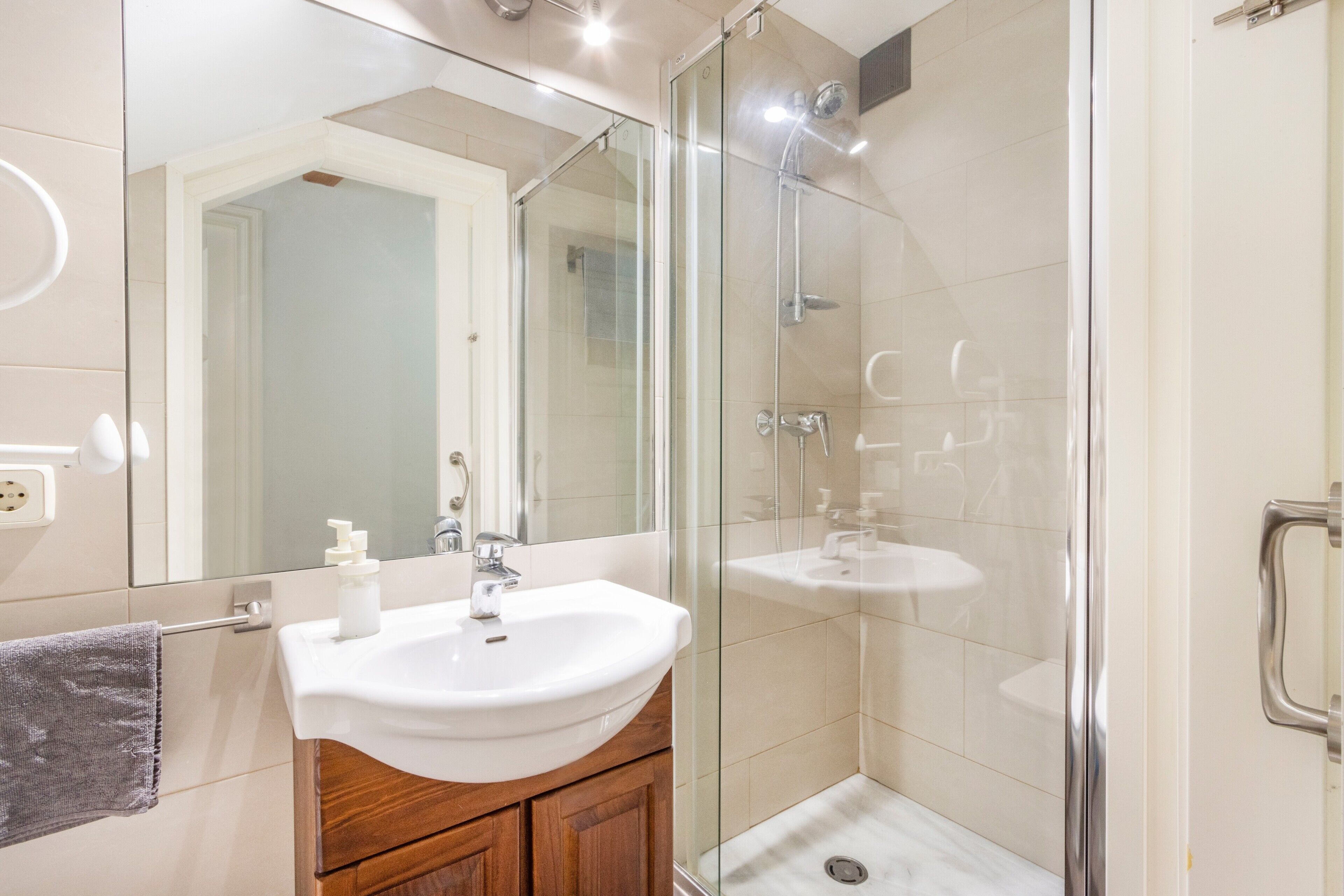 A modern bathroom with a glass shower enclosure, a white sink, and a wooden vanity.