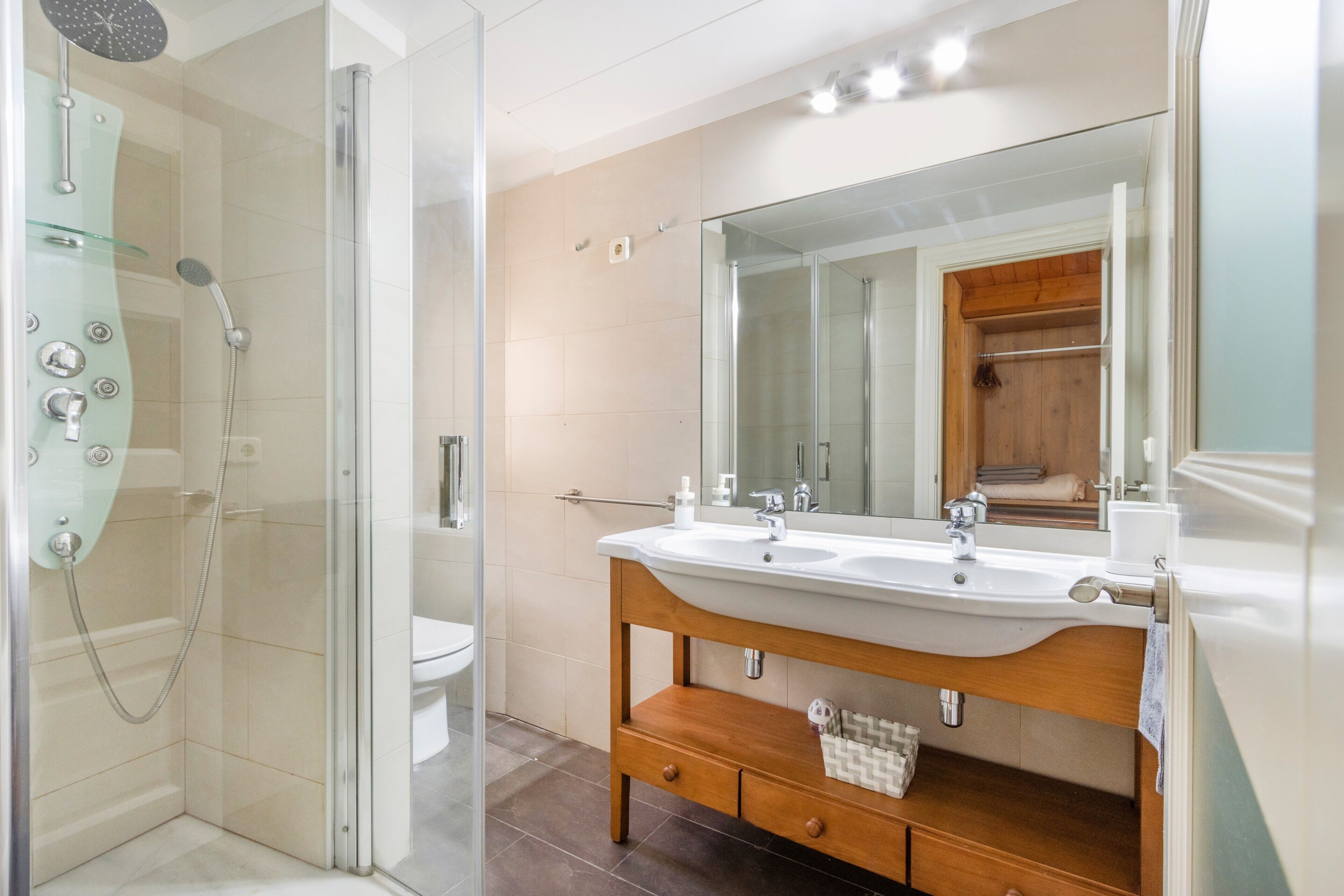 Un baño moderno con ducha de vidrio, tocador de madera con un espejo grande y un lavabo blanco.