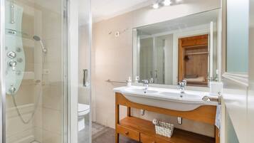 Un baño moderno con ducha de vidrio, tocador de madera con un espejo grande y un lavabo blanco.