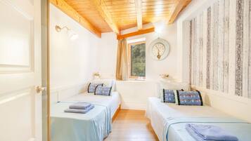 A room with two beds, a wooden ceiling, a clock on the wall, and a window with curtains.
