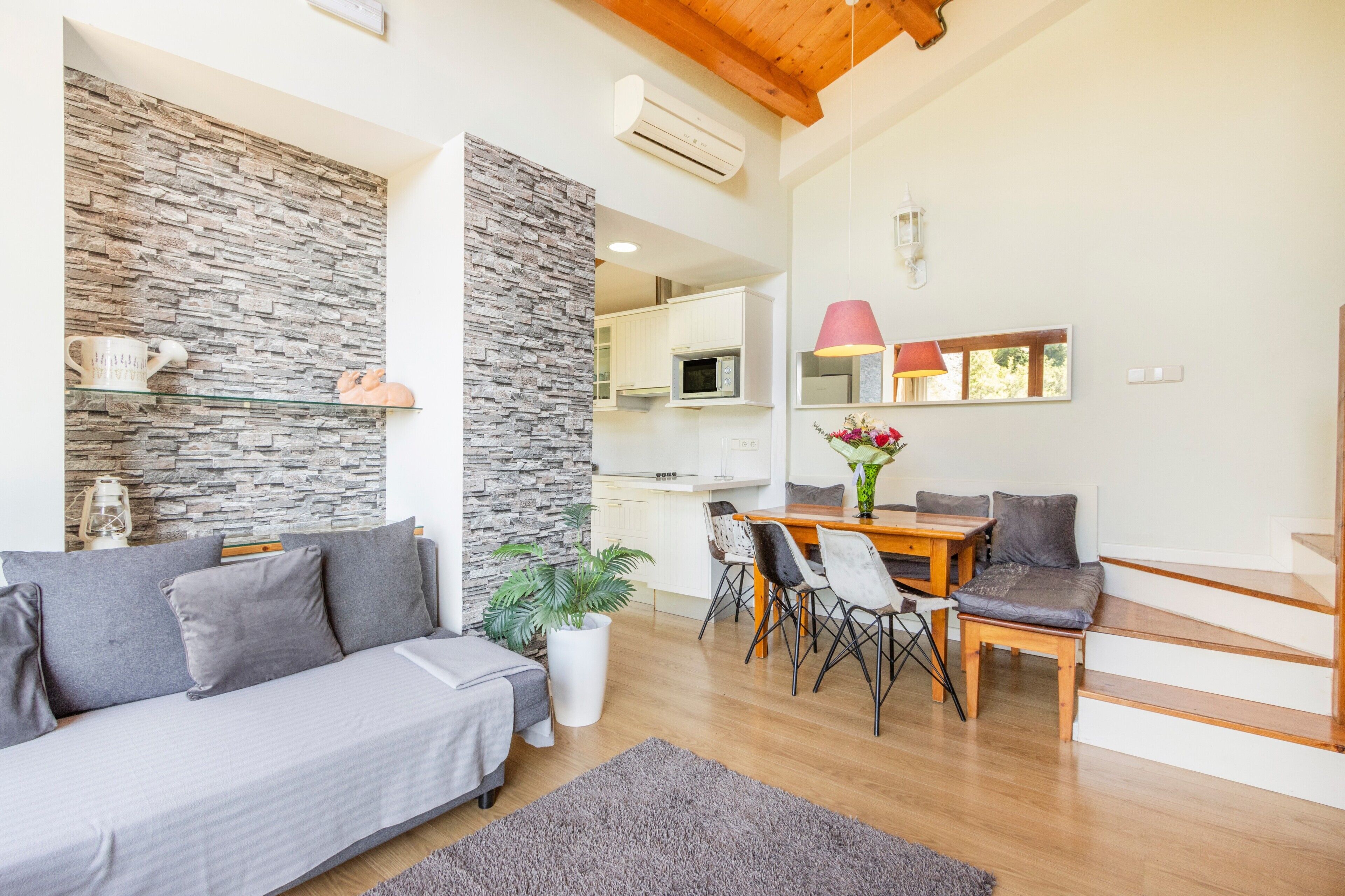 A modern living room with a sofa, dining table, chairs, a staircase, and a kitchen area.