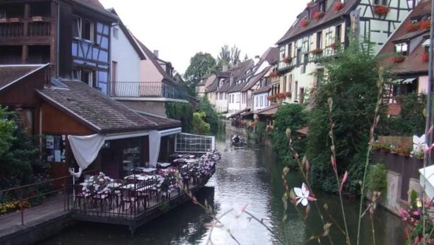 Un estrecho canal bordeado por edificios tradicionales con balcones, un restaurante con terraza y un pequeño puente.