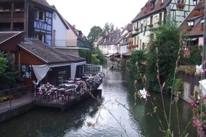 Un estrecho canal bordeado por edificios tradicionales con balcones, un restaurante con terraza y un pequeño puente.
