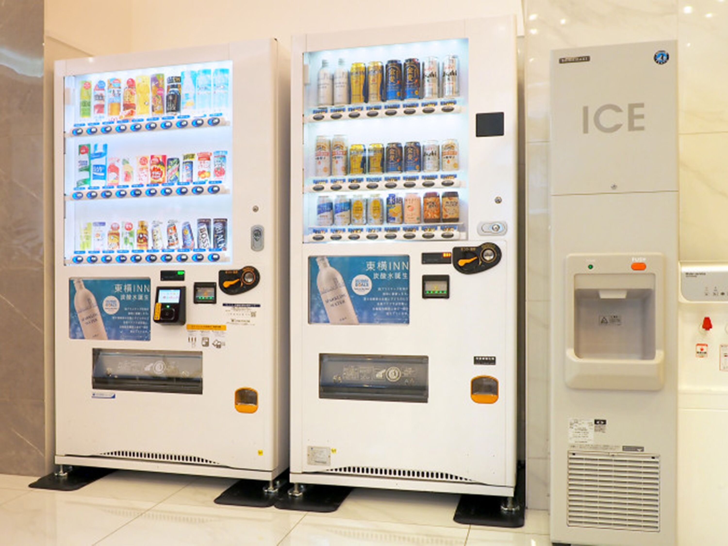 Deux distributeurs automatiques de boissons et un distributeur de glaçons, le tout installé dans un espace propre et carrelé.