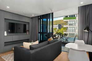 A modern living room with a large flat-screen TV, grey sofa, and a dining area with a white table and chairs. - The Avant 305 (Cape Town)