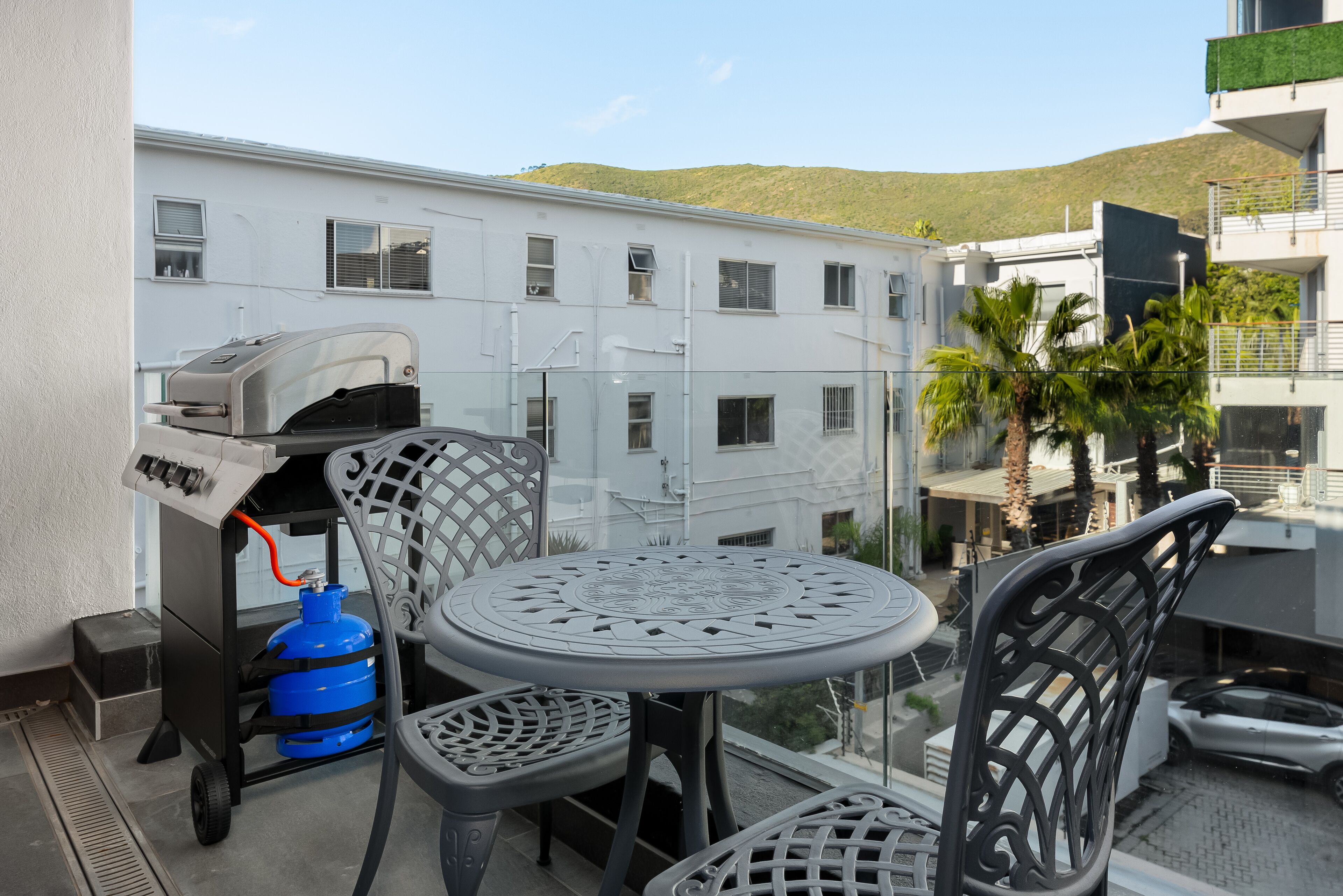 Un balcon avec un barbecue, des chaises et une table.