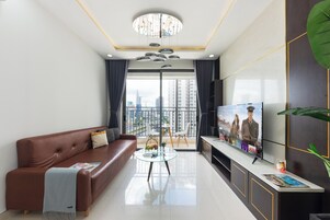 Una sala de estar moderna con un sofá de cuero marrón, una mesa de centro de vidrio, un televisor de pantalla plana y vistas a la ciudad a través de grandes ventanales.