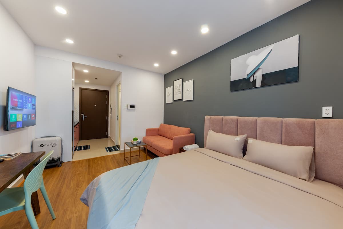 A modern hotel room with a bed, a desk, a chair, a sofa, and a television.